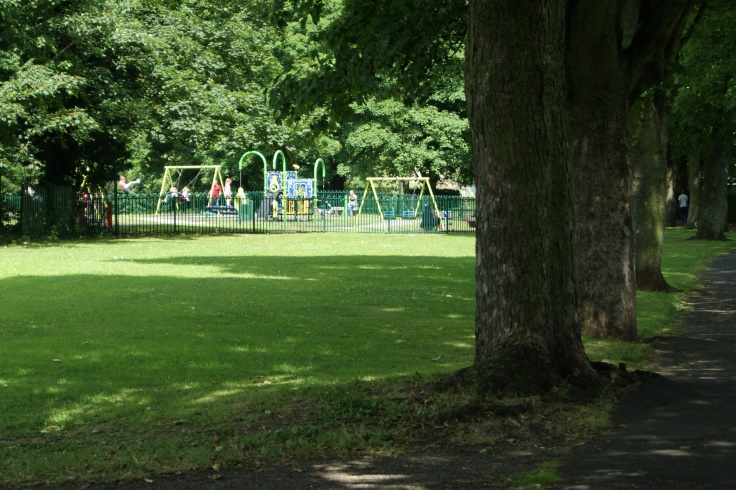 A pavement with trees and a play area on the left.